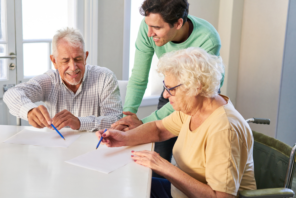 seniors filling out contracts or wills at home with the help of their son