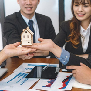 A group of business professionals holding a house model over a table during a meeting